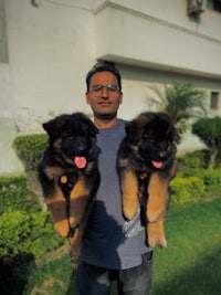 a man holding two german shepherd puppies in front of a house